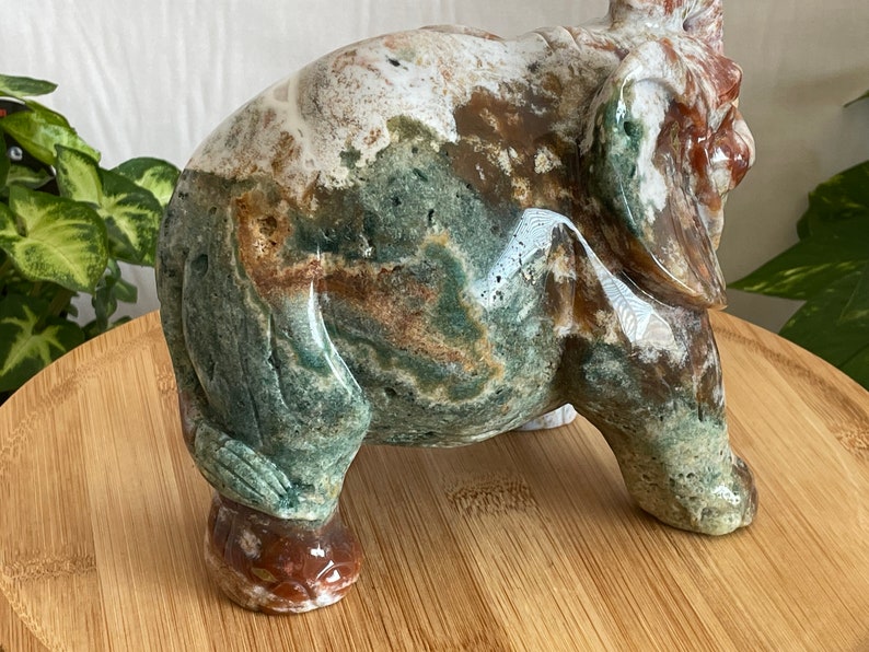 May include: A green, brown and white carved stone elephant figurine. The elephant is standing on a wooden surface.