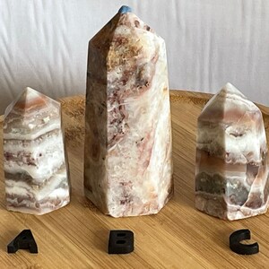 May include: Three white, brown, and pink striped crystal points on a wooden surface. The points are labeled A, B, and C.