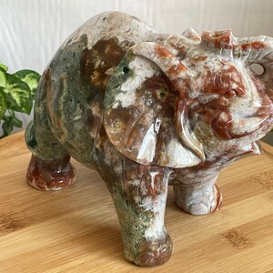 May include: A hand-carved elephant figurine made of green, brown, and white agate. The elephant is standing on a wooden surface.