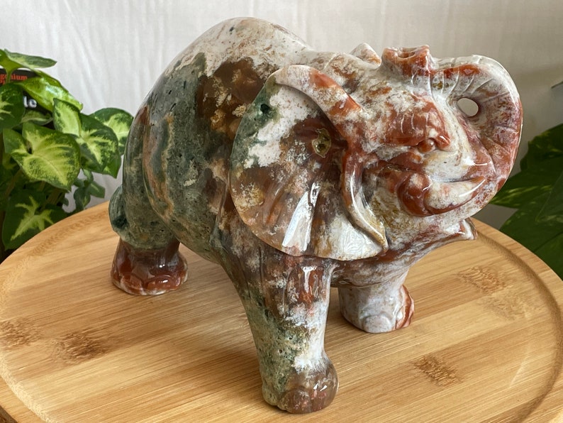May include: A hand-carved elephant figurine made of green, brown, and white agate. The elephant is standing on a wooden surface.