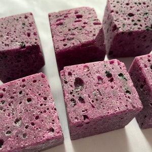 May include: Six purple and black speckled gemstone cubes. The cubes are rough and have a porous texture.