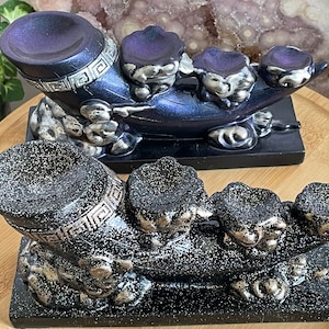 May include: Two black and silver incense holders with three small bowls on each. The holders are shaped like a dragon's head and have a sparkly finish.