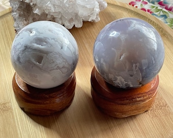 May include: Two agate spheres on wooden bases. The spheres are white and light purple with swirling patterns. The bases are a rich brown colour.