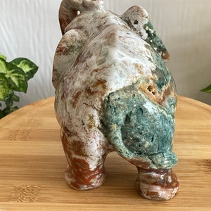 May include: A carved stone elephant figurine with a white, green, and brown marbled pattern. The elephant is standing on a wooden surface.