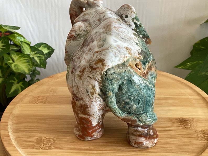 May include: A carved stone elephant figurine with a white, green, and brown marbled pattern. The elephant is standing on a wooden surface.