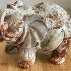 May include: A hand-carved elephant figurine made of white, brown, and red marble. The elephant is standing with its trunk raised and its head tilted to the side.