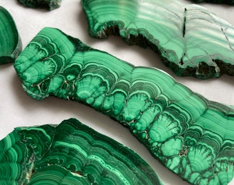 Pode incluir: Close-up de uma pedra de malaquita verde com um padrão de espiral e camadas. A pedra é lisa e polida, com uma forma natural e orgânica.