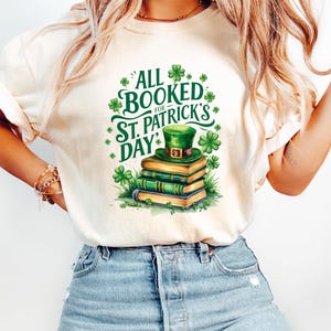 Könnte beinhalten: Ein weißes T-Shirt mit einem grünen Kleeblatt und dem Text "All Booked for St. Patrick's Day" darauf gedruckt. Ein Stapel Bücher mit einem grünen Koboldhut obenauf befindet sich in der Mitte des Designs.