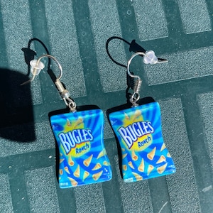 May include: A pair of silver dangle earrings with blue and yellow Bugles Ranch snack chip bag charms.