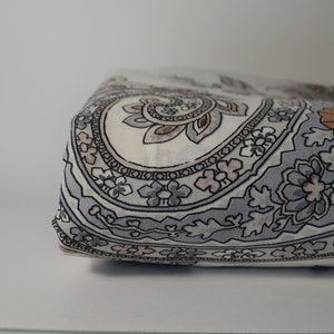May include: Close-up of a folded fabric with a paisley pattern in shades of grey, brown, and white.