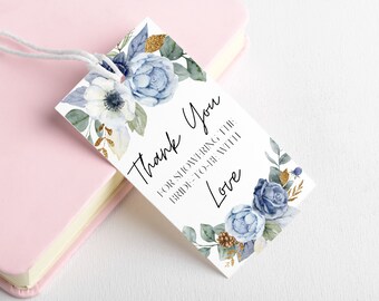 以下が含まれることがあります： 青と白の花と金のアクセントが付いた白いサンキュータグ。テキストには「花嫁に愛を込めてシャワーを浴びせてくれてありがとう」と書いてあります。