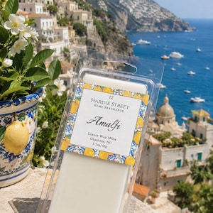 May include: A clear plastic clamshell package containing white wax melts. The label features a yellow lemon pattern and reads 12 Hardie Street Home Fragrance, Amalfi, Luxury Wax Melts, Charlotte, NC, 1.7oz/48g. The wax is rectangular and solid.