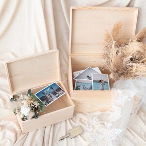 Pu&ograve; includere: Due scatole di legno aperte e non rifinite con coperchi, una contenente foto e fiori secchi. L'altra scatola contiene foto e un'etichetta in pelle che dice "Let the adventure begin". Sono presenti anche un bouquet di fiori secchi e un velo di pizzo bianco.