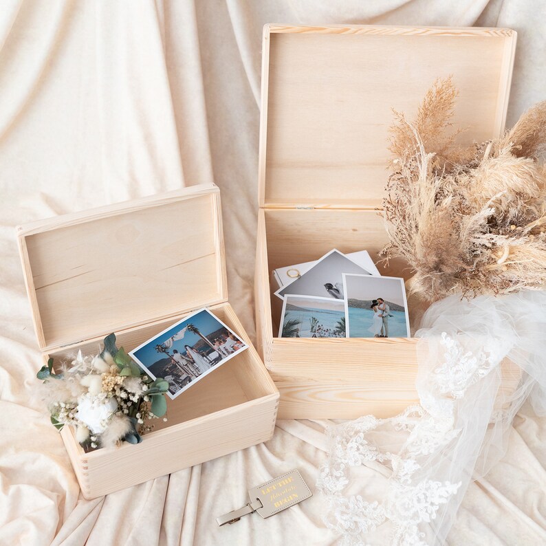 Pu&ograve; includere: Due scatole di legno aperte e non rifinite con coperchi, una contenente foto e fiori secchi. L'altra scatola contiene foto e un'etichetta in pelle che dice "Let the adventure begin". Sono presenti anche un bouquet di fiori secchi e un velo di pizzo bianco.