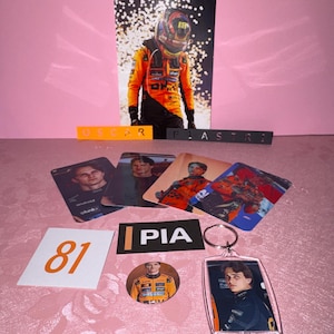Puede incluir: Una colecci&oacute;n de merchandising de fans con un piloto de F&oacute;rmula 1. Incluye una foto grande, cromos, un llavero, un bot&oacute;n y un letrero con el n&uacute;mero 81. Los art&iacute;culos son de color naranja, negro y blanco.