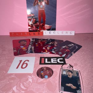 Puede incluir: Una colecci&oacute;n de recuerdos de Charles Leclerc, que incluye una foto suya con un traje de carreras rojo, un llavero, una chapa y varias tarjetas. El n&uacute;mero 16 se muestra en un cuadrado blanco, y el nombre "CHARLES LECLERC" est&aacute; escrito.