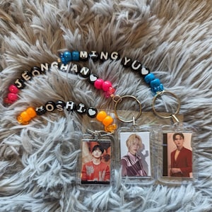 May include: Three keychains with clear acrylic photo holders and beaded name straps. The straps feature names spelled out in white letter beads and colorful accent beads. Each keychain has a different photo.