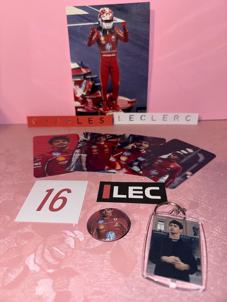 Puede incluir: Una colecci&oacute;n de recuerdos de Charles Leclerc, que incluye una tarjeta fotogr&aacute;fica, pegatinas, un bot&oacute;n y un llavero. Los art&iacute;culos presentan im&aacute;genes de Leclerc con su traje de carreras y el n&uacute;mero 16. El fondo es un estampado floral rosa.