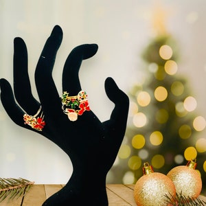 May include: A black hand model wearing three gold rings with red and green enamel Christmas-themed designs.