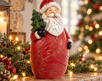 May include: A Santa Claus figurine with a red hat and coat featuring a distressed wood grain texture. The figure has a white beard, black gloves, and holds a small green Christmas tree. The design includes a white pom-pom on the hat.