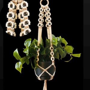 May include: A macrame plant hanger with a wooden ring at the top. The hanger is made with natural twine and has black beads woven into the design. A green plant is hanging in the planter.