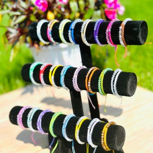 May include: A display of colorful beaded bracelets on black stands. The bracelets are made with various colors of beads, including clear, white, blue, green, yellow, orange, red, and purple.