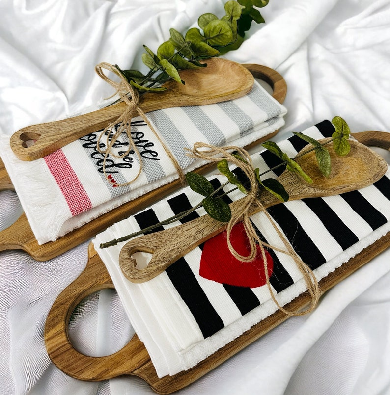 May include: Two wooden cutting boards with handles, each wrapped with a kitchen towel and a wooden spoon. One towel is gray and white striped with the text "I still get giddy" and the other is black and white striped with a red heart.