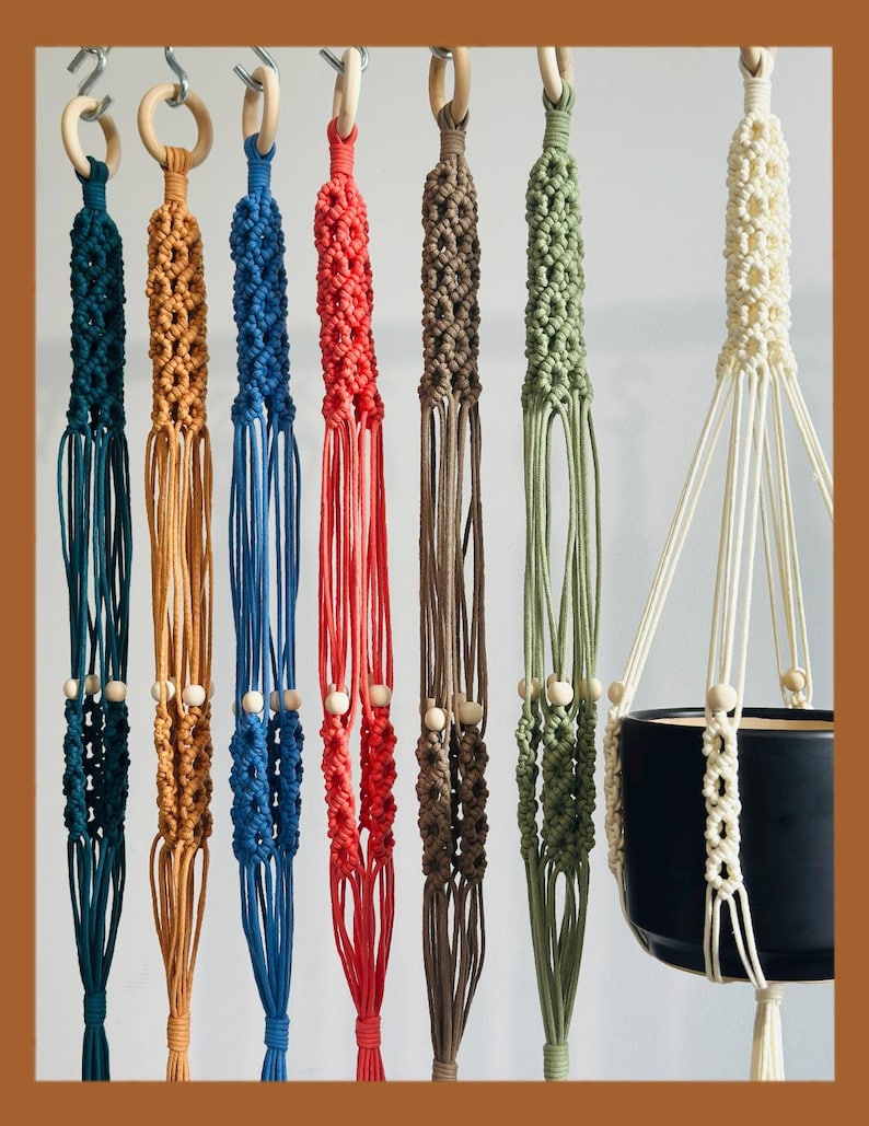 May include: A collection of macrame plant hangers in various colors, including teal, orange, blue, red, brown, and green. Each hanger features a wooden ring at the top and wooden beads. One hanger holds a black ceramic pot.