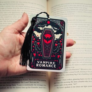 May include: A black bookmark with a tassel, featuring a coffin and bat design with the words "VAMPIRE ROMANCE". The bookmark has a black background with red hearts and bats.