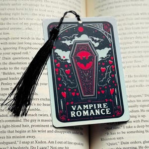 May include: A rectangular bookmark with a black tassel. The bookmark features a coffin design with a bat, hearts, and the words "VAMPIRE ROMANCE" in white. The background is black with red accents.