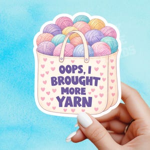Può includere: Un adesivo con una borsa tote beige piena di gomitoli colorati in rosa, viola, giallo e blu. La borsa ha un manico ed è decorata con cuori rosa. Il testo recita "Oops, I brought more yarn."