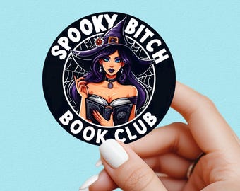 May include: A round black sticker with the words "SPOOKY BITCH BOOK CLUB" encircling an illustration of a witch with purple hair and a witch hat. The witch is holding a book and has blue eyes. A spider web design is behind the witch.