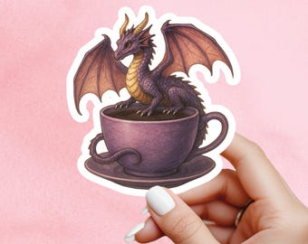 May include: A sticker featuring a purple dragon perched inside a purple teacup filled with a dark liquid. The dragon has large, outstretched wings and yellow horns. The teacup sits on a matching saucer, all against a pink background.