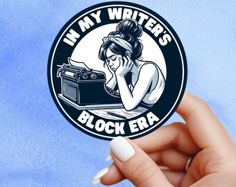 May include: A round sticker with a black border and the text "IN MY WRITER'S BLOCK ERA". The sticker features a black and white illustration of a woman resting her head on her hands in front of a typewriter.
