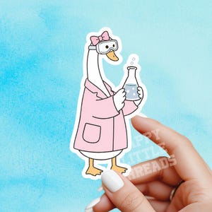 May include: A die-cut sticker featuring a white goose wearing a pink lab coat, a pink bow on its head, and clear safety goggles. The goose is holding a glass Erlenmeyer flask filled with a light blue liquid with bubbles rising from the top.