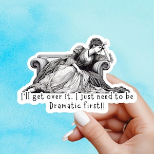 May include: A sticker with a monochrome illustration of a woman in historical dress reclining on a chaise longue. The text says, "I'll get over it. I just need to be Dramatic first!!"
