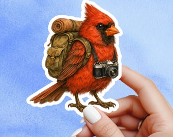 May include: A sticker depicting a red cardinal bird with a black mask and orange beak, carrying a backpack and a camera. The illustration has a detailed, adventurous theme, set against a light blue background.