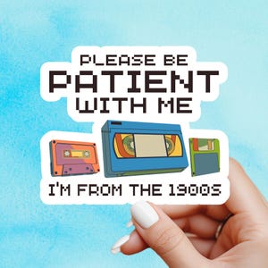 May include: A sticker with the text "PLEASE BE PATIENT WITH ME I'M FROM THE 1900S". The sticker features illustrations of a cassette tape, a VHS tape, and a floppy disk, all in retro colours against a blue background.