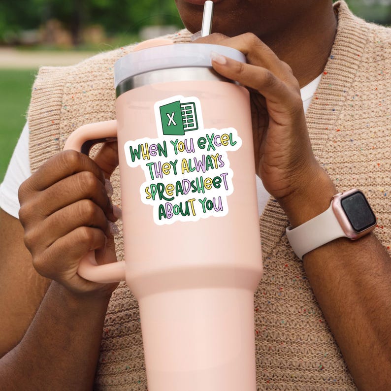 Pu&ograve; includere: Un grande bicchiere termico rosa chiaro con coperchio e manico bianchi. Un adesivo sul bicchiere presenta il logo di Microsoft Excel e il testo "When You Excel They Always Spreadsheet About You" in verde, viola e bianco.