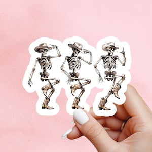 May include: A sticker featuring three dancing skeletons wearing cowboy hats and boots. The skeletons are in various poses, with one pointing and others with their hands up. The sticker has a white border and is set against a pink background.