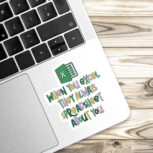 Pu&ograve; includere: Un adesivo bianco su un laptop con il logo di Microsoft Excel e il testo "When You Excel They Always Spreadsheet About You" in vari colori. Il laptop &egrave; su una superficie di legno.