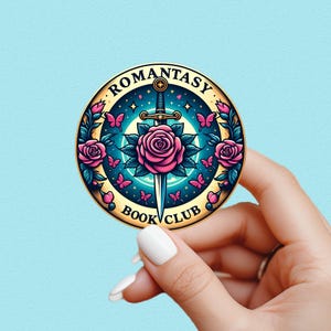 May include: A round sticker with the text "ROMANTASY BOOK CLUB" encircling a central design. The design features a sword piercing a pink rose, surrounded by pink butterflies and teal leaves, set against a teal and gold background.