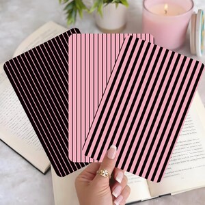 Peut inclure: Trois cartes rectangulaires à rayures verticales noires et roses. Une carte a des rayures noires, une autre a des rayures roses et la troisième a des rayures noires diagonales sur fond rose. Les cartes sont présentées sur un livre ouvert.