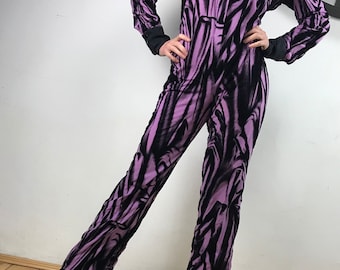 May include: A purple and black jumpsuit with a long-sleeved shirt and a button-up front. The jumpsuit has a flowing, loose fit and a unique abstract print.