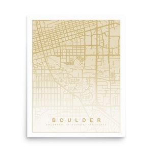 May include: A gold-toned map of Boulder, Colorado, with a white background. The map shows the city's streets and landmarks. The text "BOULDER" is printed in large letters at the bottom of the map, with the text "COLORADO - 40.0148° N - 105.2725° W" printed in smaller letters below.