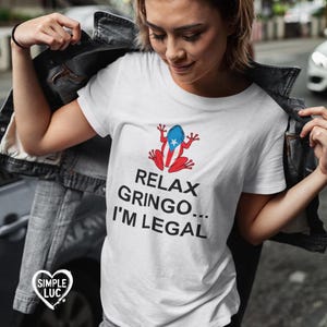 May include: White t-shirt with a cartoon frog wearing a Puerto Rican flag. The text on the shirt reads "Relax Gringo... I'm Legal."