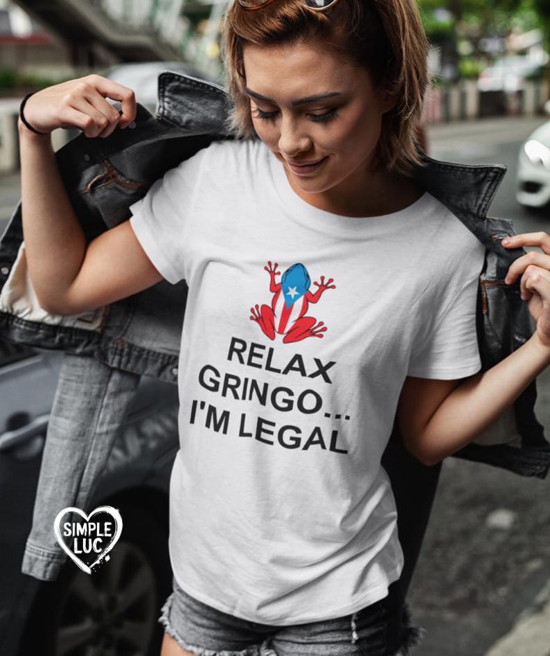 May include: White t-shirt with a cartoon frog wearing a Puerto Rican flag. The text on the shirt reads "Relax Gringo... I'm Legal."