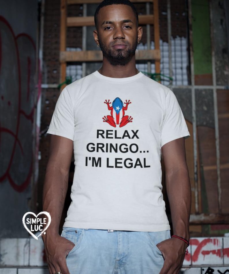 May include: White t-shirt with a red and blue frog wearing a Puerto Rican flag. The text on the shirt reads "Relax Gringo... I'm Legal."