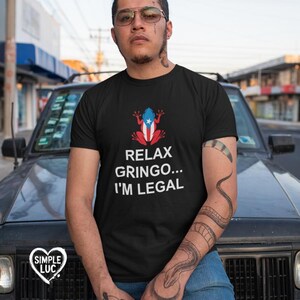 May include: Black t-shirt with a white frog wearing a Puerto Rican flag. The text "Relax Gringo... I'm Legal" is printed on the shirt.