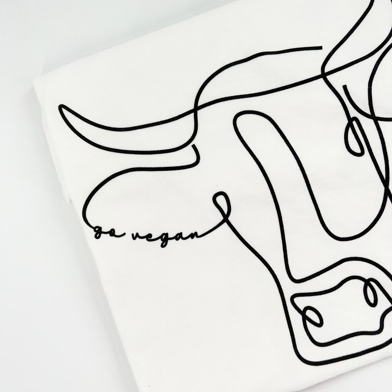 May include: A white t-shirt with a black line drawing of a cow's head. The text "go vegan" is written below the cow's head.